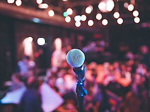 Mikrophoneständer auf einer Bühne vor verschwommen dargestelltem Publikum