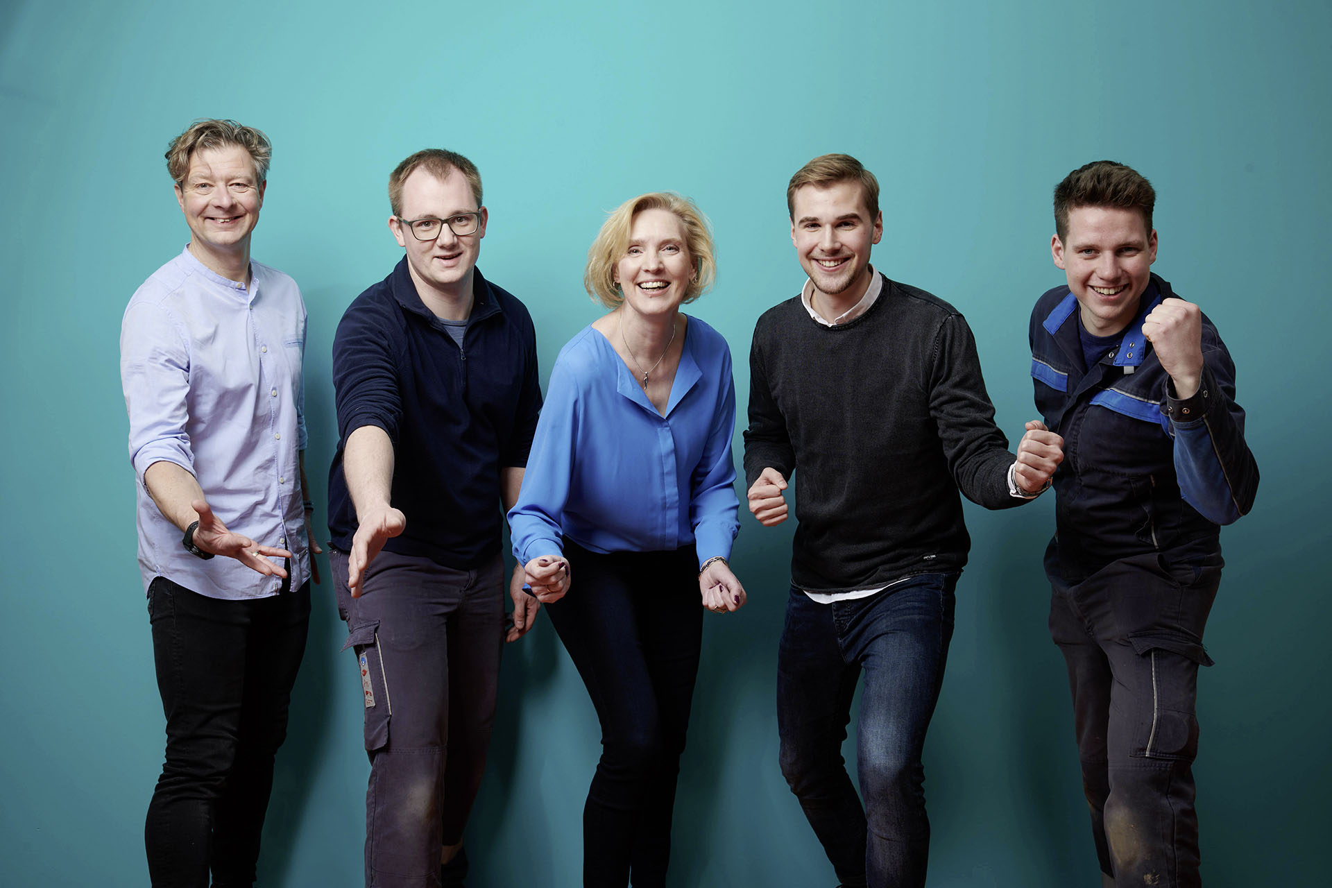 WW Bewerber Gruppenbild von motivierten Personen vor einem petrolfarbenen Hintergrund
