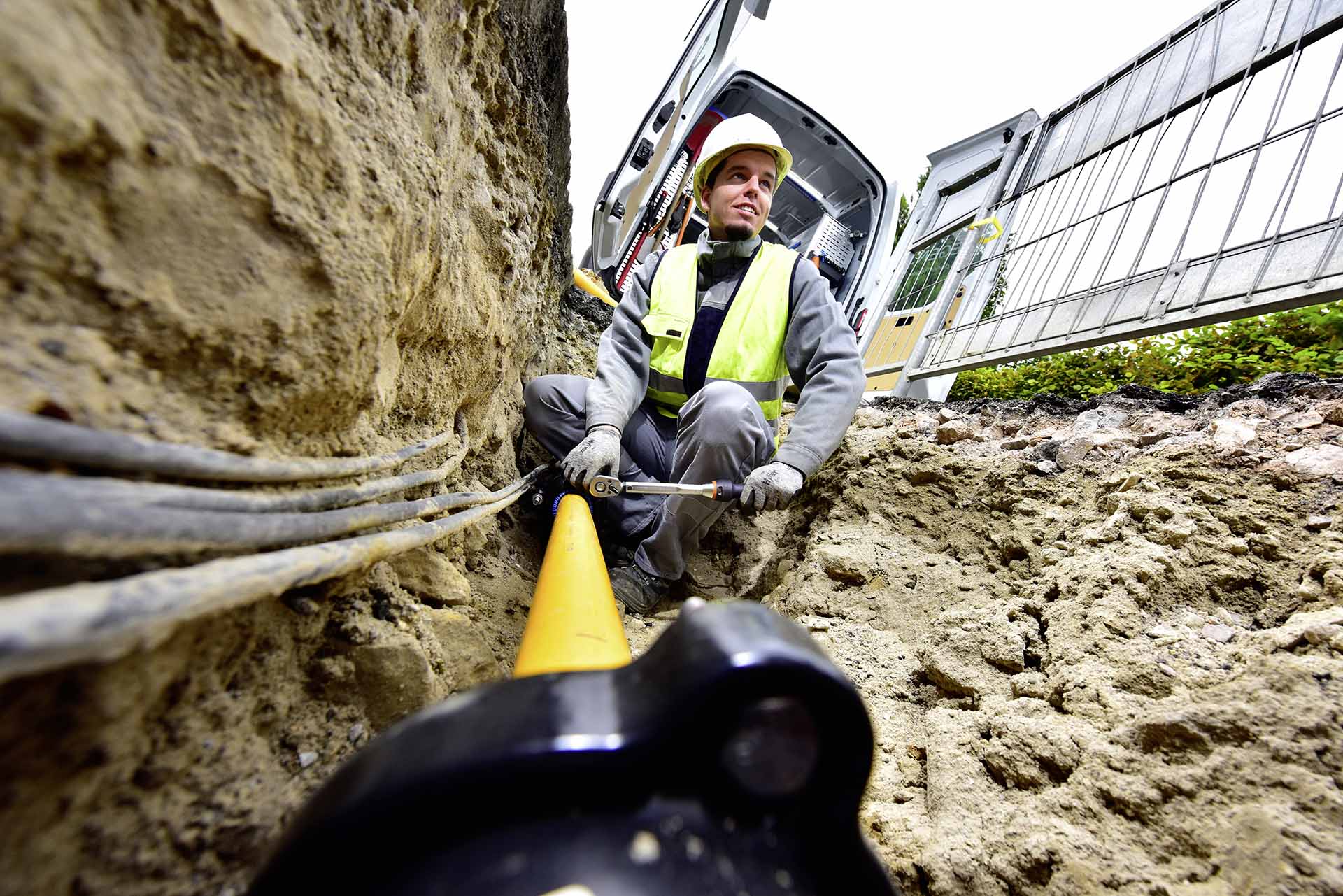 WWN Netzdienstleistungen Monteur in einem Kabelgraben mit Warnweste und Helm