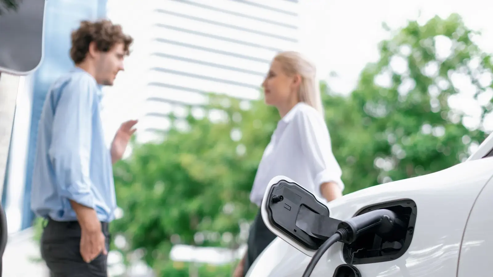 Ladehardware für vernetztes E‑Mobilitätsladen Zwei Personen stehen neben einem ladenden Elektroauto und sprechen miteinander.