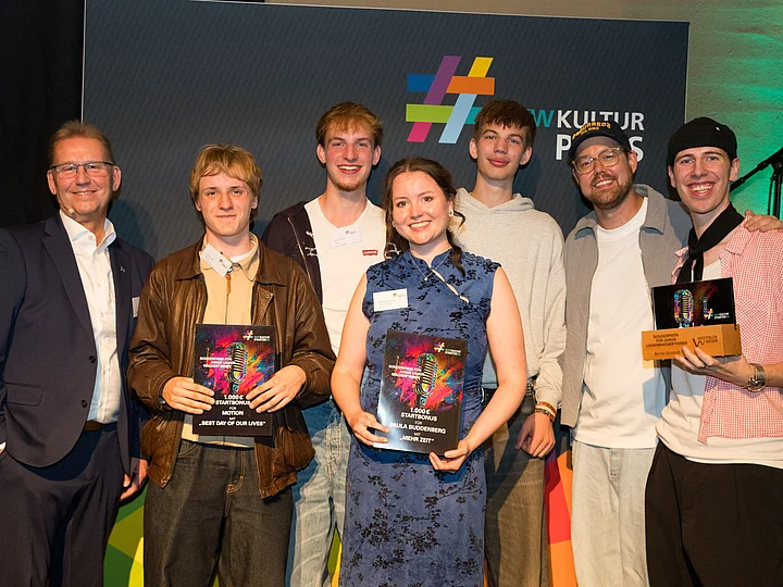 Gruppenfoto aller ausgezeichneten KulturSTARTER mit Urkunden und Auszeichnungen vor der Fotowand der Preisverleihung.