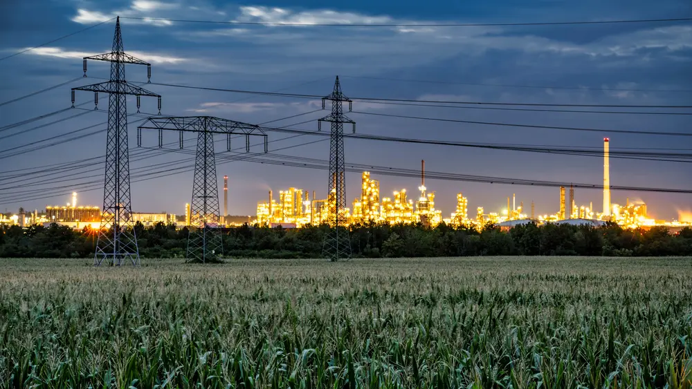 Strommasten und Hochspannungsleitungen führen zu einer beleuchteten Industrieanlage bei Dämmerung.