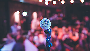 Mikrophoneständer auf einer Bühne vor verschwommen dargestelltem Publikum