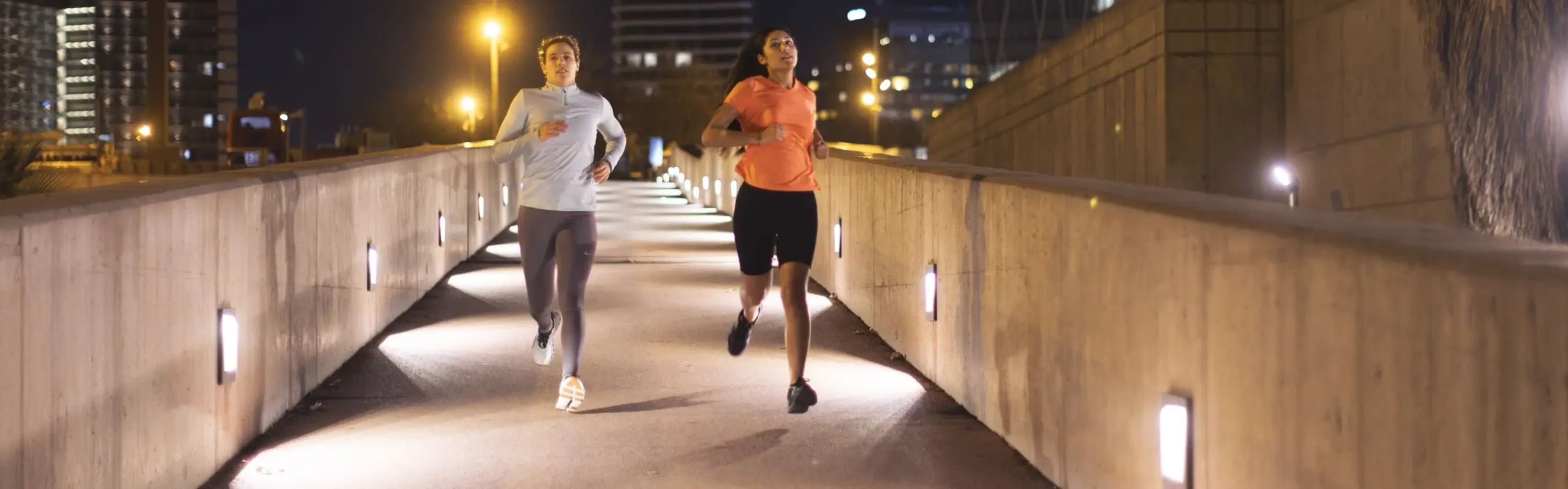 Zwei Jogger rennen über eine beleuchtete Brücke.