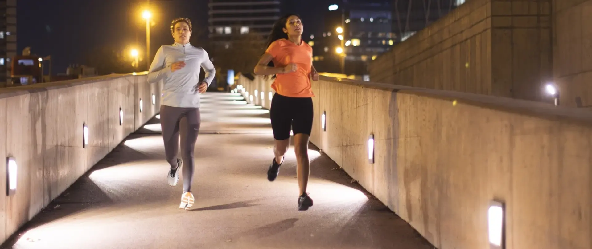 Zwei Jogger rennen über eine beleuchtete Brücke.
