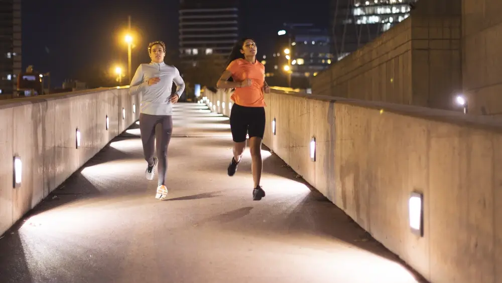 Zwei Jogger rennen über eine beleuchtete Brücke.