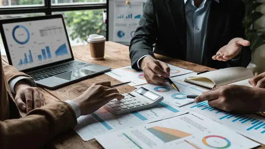 Bilanzkreismanagement von erneuerbaren Energien Drei Personen sitzen an einem Tisch, auf dem Zettel sowie ein Laptop mit Diagrammen und Statistiken liegen, und besprechen diese.
