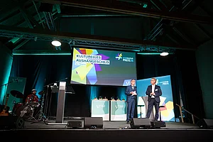 Jürgen Noch und Ingo Börchers auf der Bühne Moderation von Ingo Börchers und Jürgen Noch auf der Bühne vor einem großem Veranstaltungsbildschirm und Hauptpreisen.