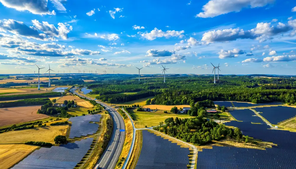Eine Luftaufnahme zeigt Windräder und Solarfelder in der Landschaft bei klarem Himmel.