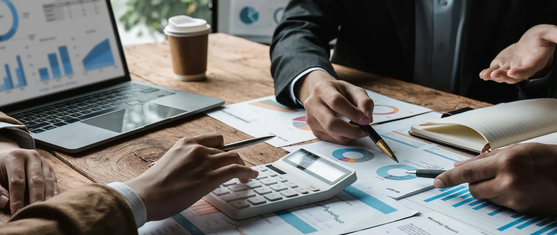 Drei Personen sitzen an einem Tisch, auf dem Blätter mit verschiedenen Statistiken liegen ebenso wie ein Laptop.