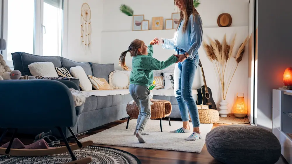 Eine Mutter tanzt mit ihrer Tochter in einem schön eingerichteten Wohnzimmer