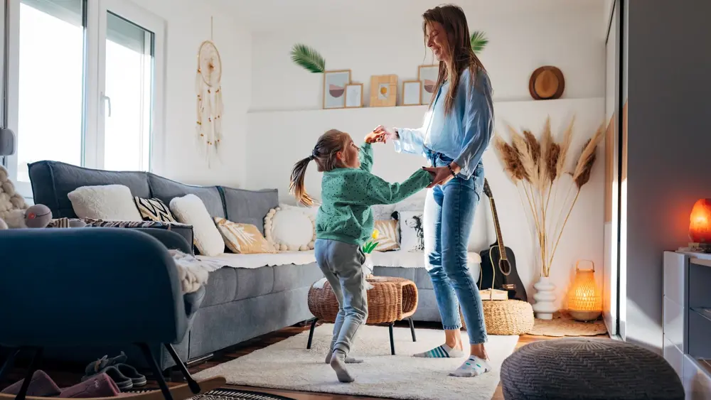 Eine Mutter tanzt mit ihrer Tochter in einem schön eingerichteten Wohnzimmer