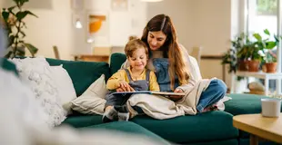 Mutter und Sohn sitzen gemütlich auf dem Sofa und schauen sich ein Bilderbuch an. Das Wohnzimmer ist mit Pflanzen dekorativ geschmückt