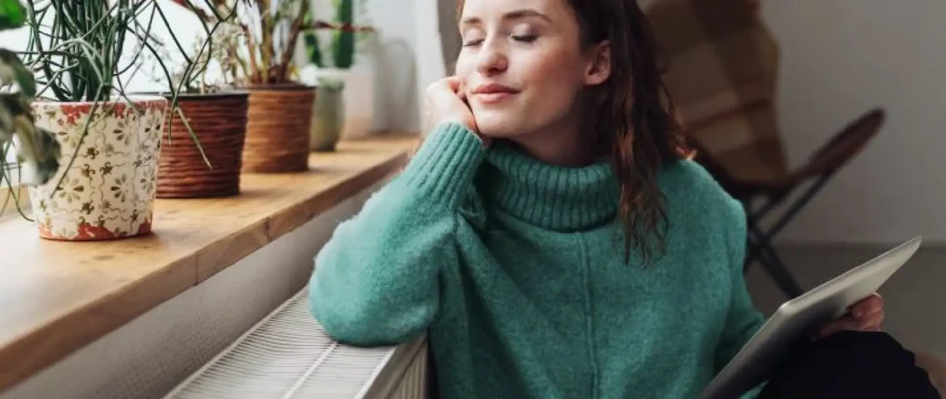 Frau sitzt im beheizten Wohnzimmer und lehnt auf der Fensterbank