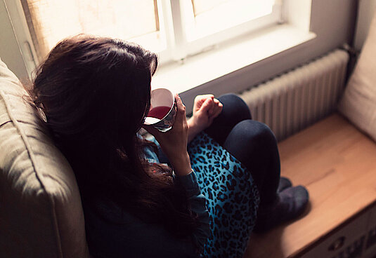 Frau sitzt auf der Fensterbank und trinkt einen Tee