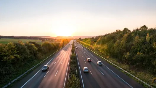 Autos fahren auf einer von Bäumen umgebenen Autobahn bei Sonnenuntergang in beide Richtungen.
