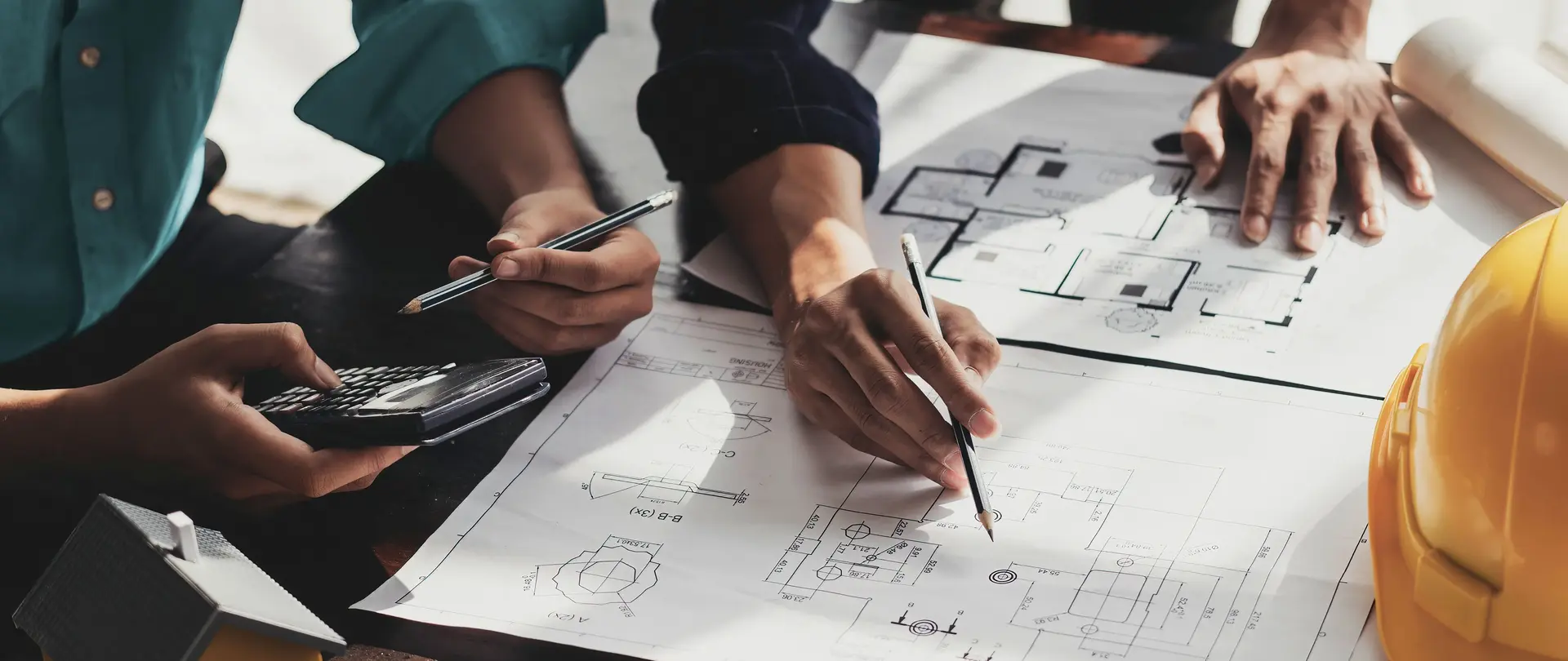 Zwei Planer arbeiten an einem Tisch mit Anlagenplänen an einem maßgeschneiderten Konzept zur Schutz- und Sekundärtechnik von Anlagen.