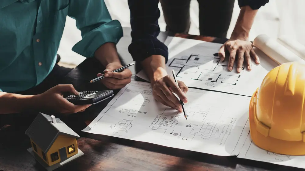 Zwei Planer arbeiten an einem Tisch mit Anlagenplänen an einem maßgeschneiderten Konzept zur Schutz- und Sekundärtechnik von Anlagen.