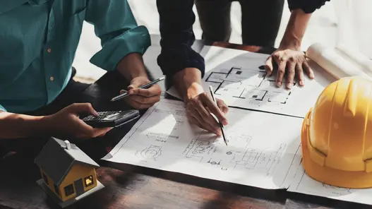 Zwei Planer arbeiten an einem Tisch mit Anlagenplänen an einem maßgeschneiderten Konzept zur Schutz- und Sekundärtechnik von Anlagen.