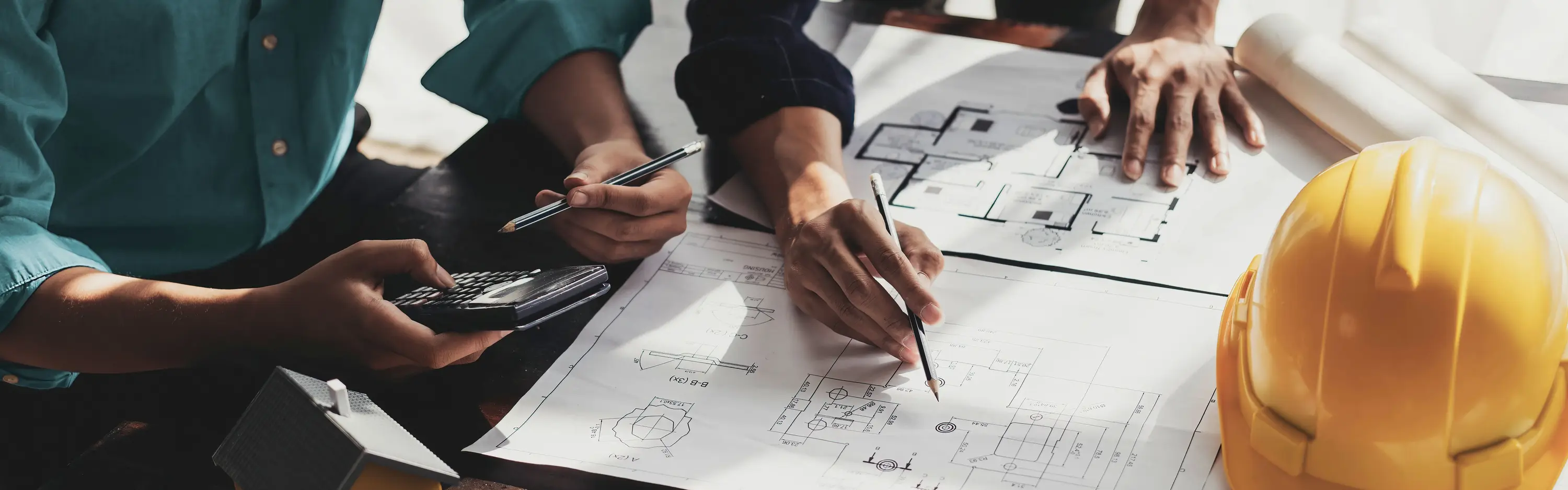 Zwei Planer arbeiten an einem Tisch mit Anlagenplänen an einem maßgeschneiderten Konzept zur Schutz- und Sekundärtechnik von Anlagen.