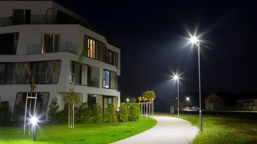 Ein modernes Wohngebäude bei Nacht mit beleuchtetem Weg und Straßenlaternen.