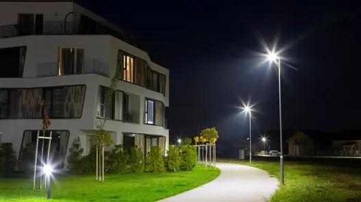 Ein modernes Wohngebäude bei Nacht mit beleuchtetem Weg und Straßenlaternen.