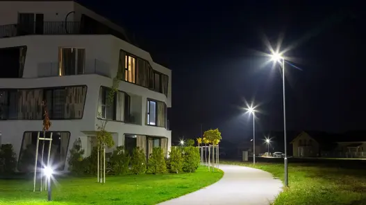 Ein modernes Wohngebäude bei Nacht mit beleuchtetem Weg und Straßenlaternen.