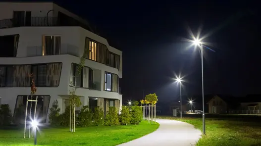 Ein modernes Wohngebäude bei Nacht mit beleuchtetem Weg und Straßenlaternen.