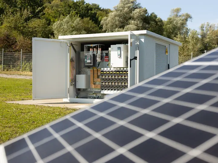 Eine offene Trafostation ist samt der Technik im Hintergrund einer Photovoltaikanlage zu sehen.