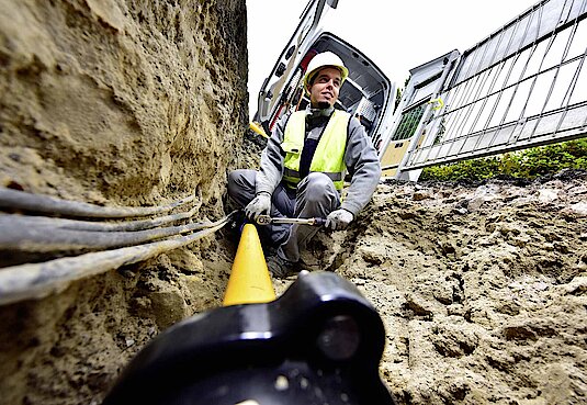 Monteur in einem Kabelgraben mit Warnweste und Helm