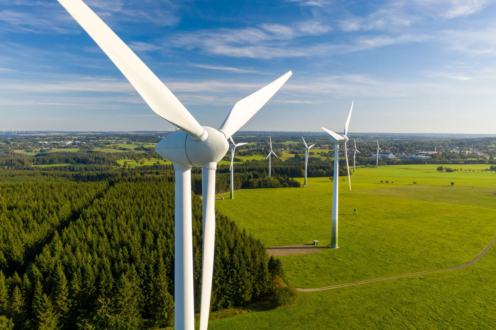 Mehrere Windkraftanlagen stehen auf grünen Wiesen unter blauem Himmel mit vereinzelten Wolken.