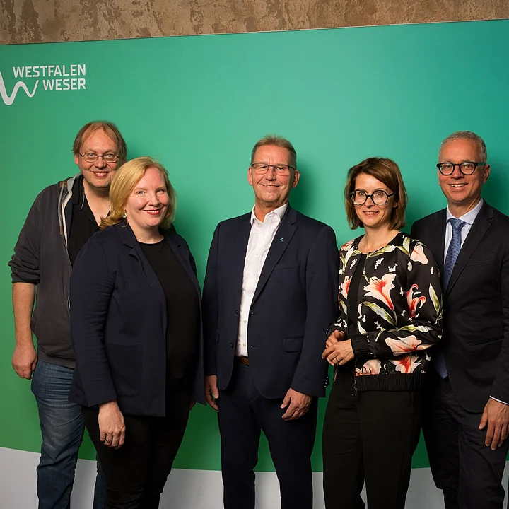 Die Jurymitglieder Sechs Mitglieder der Jury vom WWKulturSTARTER26 stehen vor einer grünen Westfalen-Weser-Fotowand.