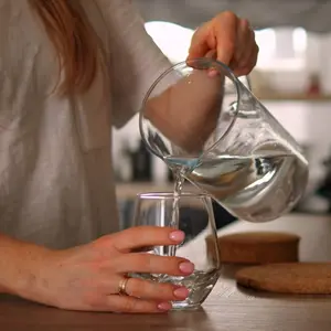 Eine Frau steht in der Küche an der Arbeitsfläche und füllt dabei Wasser aus einer Karaffe in ein Glas