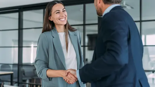 Zwei Personen in Businesskleidung geben sich in einem modernen Büro die Hand.