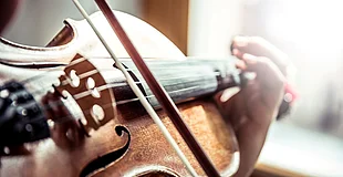 Man sieht eine Geige, einen Streicher und eine Hand, die etwas unscharf ist
