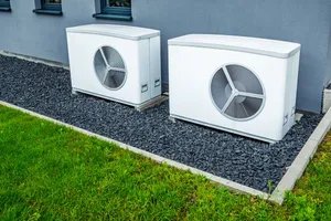 Zwei weiße und identische Luftwärmepumpen im Garten auf Kies stehend