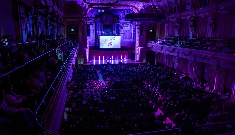 Konzertsaal in Wuppertal während der NightWash Geburtstagtour. Der Saal ist pompös und lila ausgeleuchtet. Alle Plätze sind ausgebucht.