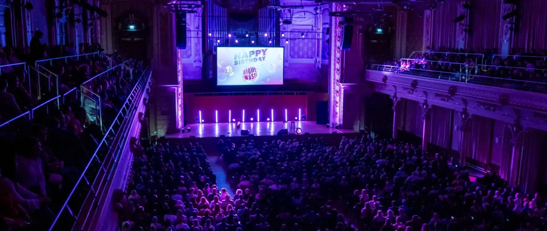 Konzertsaal in Wuppertal während der NightWash Geburtstagtour. Der Saal ist pompös und lila ausgeleuchtet. Alle Plätze sind ausgebucht.