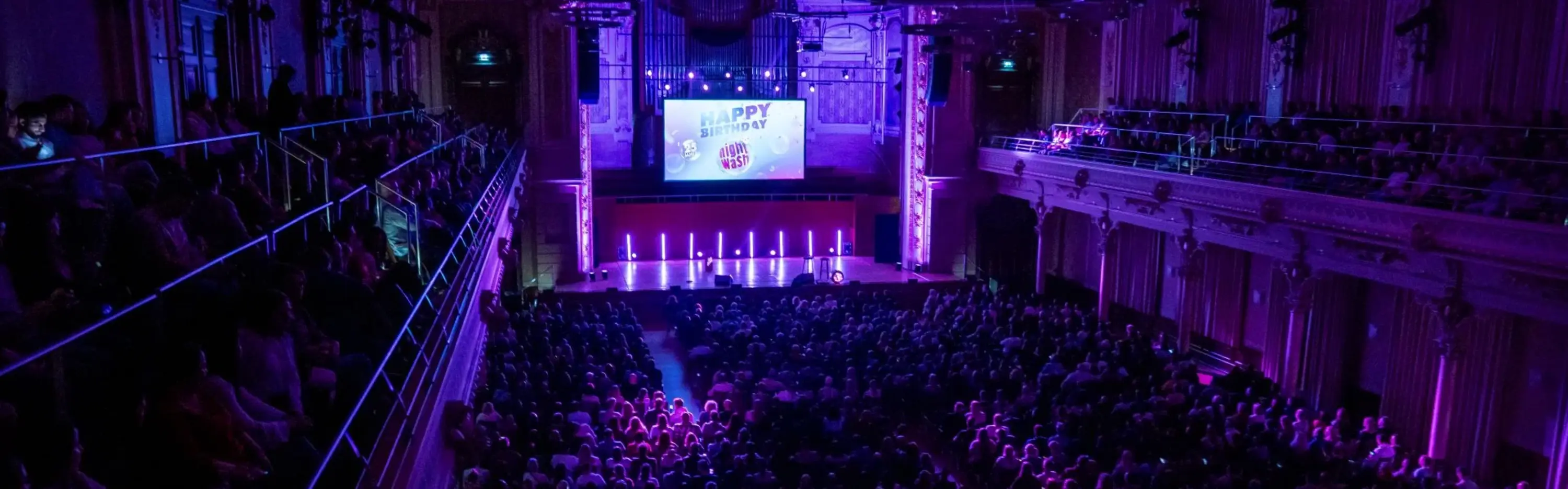 Konzertsaal in Wuppertal während der NightWash Geburtstagtour. Der Saal ist pompös und lila ausgeleuchtet. Alle Plätze sind ausgebucht.