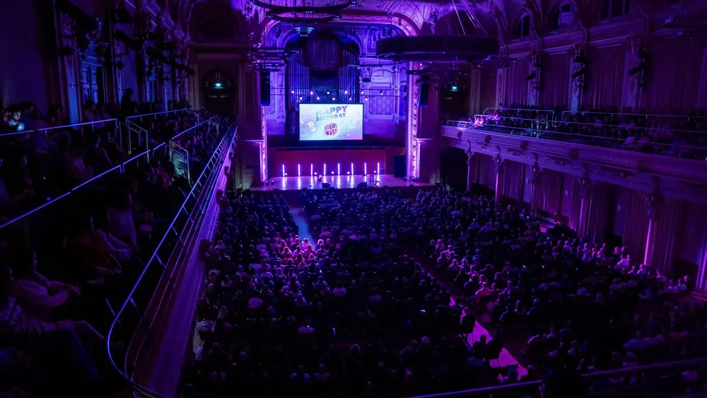 Konzertsaal in Wuppertal während der NightWash Geburtstagtour. Der Saal ist pompös und lila ausgeleuchtet. Alle Plätze sind ausgebucht.