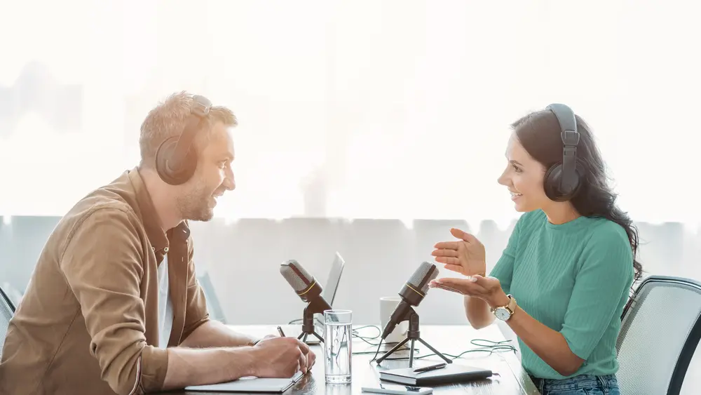 Ein Mann und eine Frau sitzen sich gegenüber und nehmen einen Podcast auf