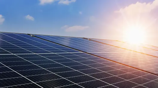 Eine große Fläche von Solarpaneelen reflektiert Sonnenlicht unter blauem Himmel mit wenigen Wolken.