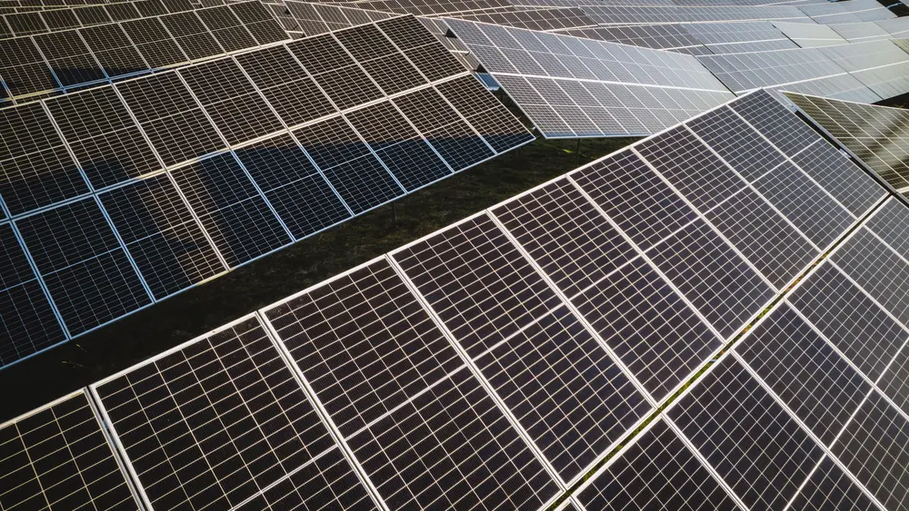 Ein großer Solarpark mit vielen Photovoltaikanlagen befindet sich auf einem Feld in der Sonne.