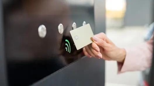 Eine Person hält eine Chipkarte an ein Terminal mit Kontaktlos-Symbol zur Abrechnung von Ladevorgängen.