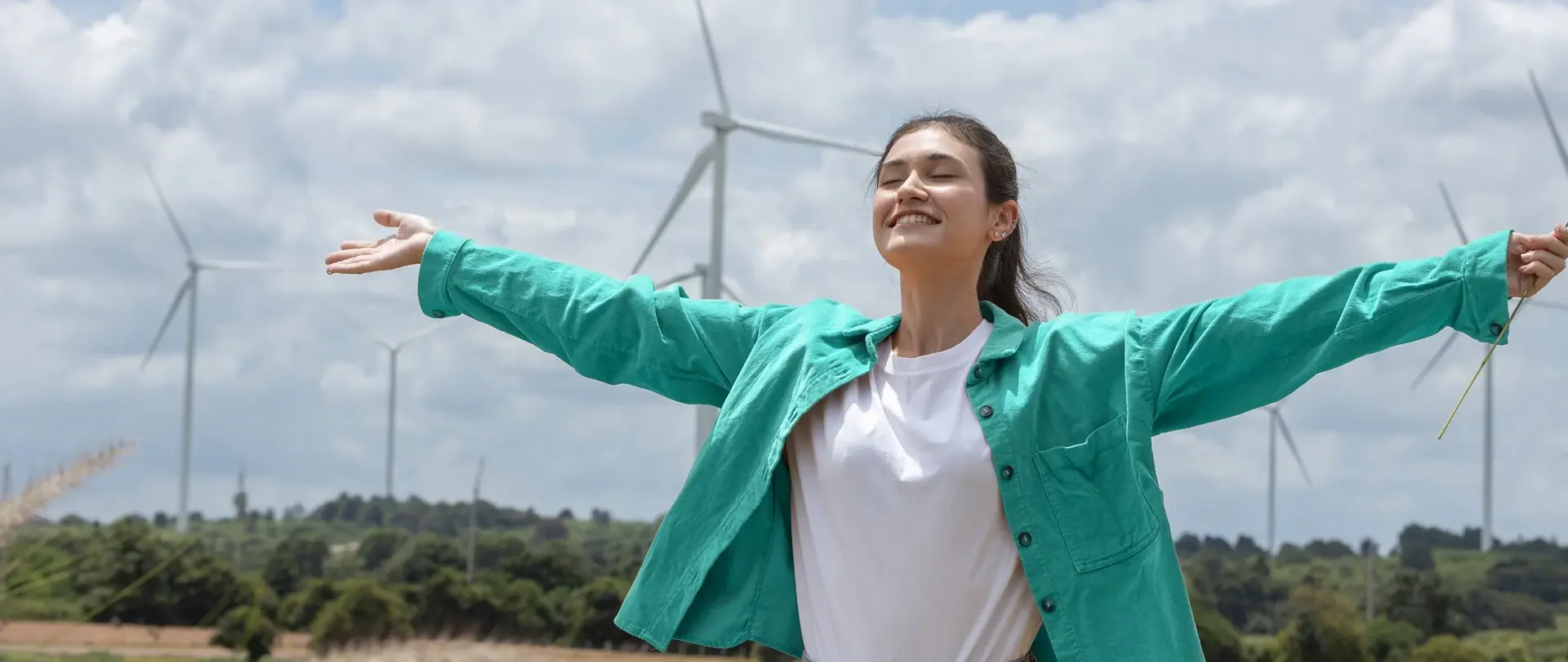 Junge Frau genießt die Sonne und im Hintergrund sind Windräder.