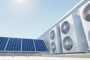 Auf dem Dach eines Industriegebäudes stehen mehrere Wärmepumpen neben einer großen Photovoltaik-Anlage. Die Sonne scheint und der Himmel ist blau