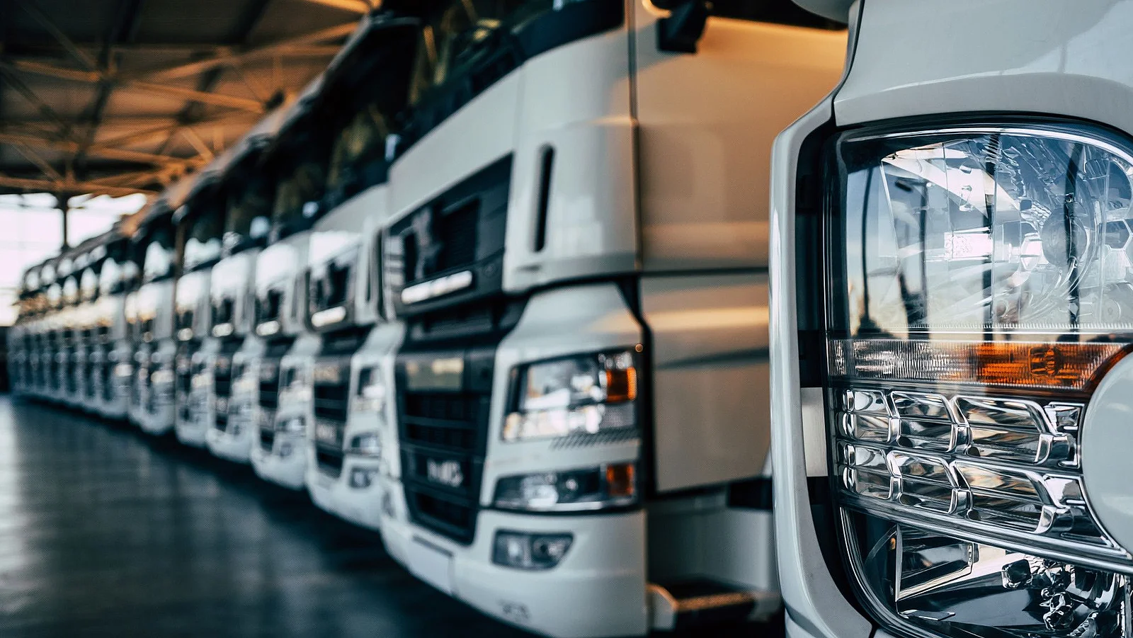 Elektrische LKW-Flotten für effiziente Logistikprozesse Mehrere moderne LKW stehen in einer Reihe in einer Fahrzeughalle.