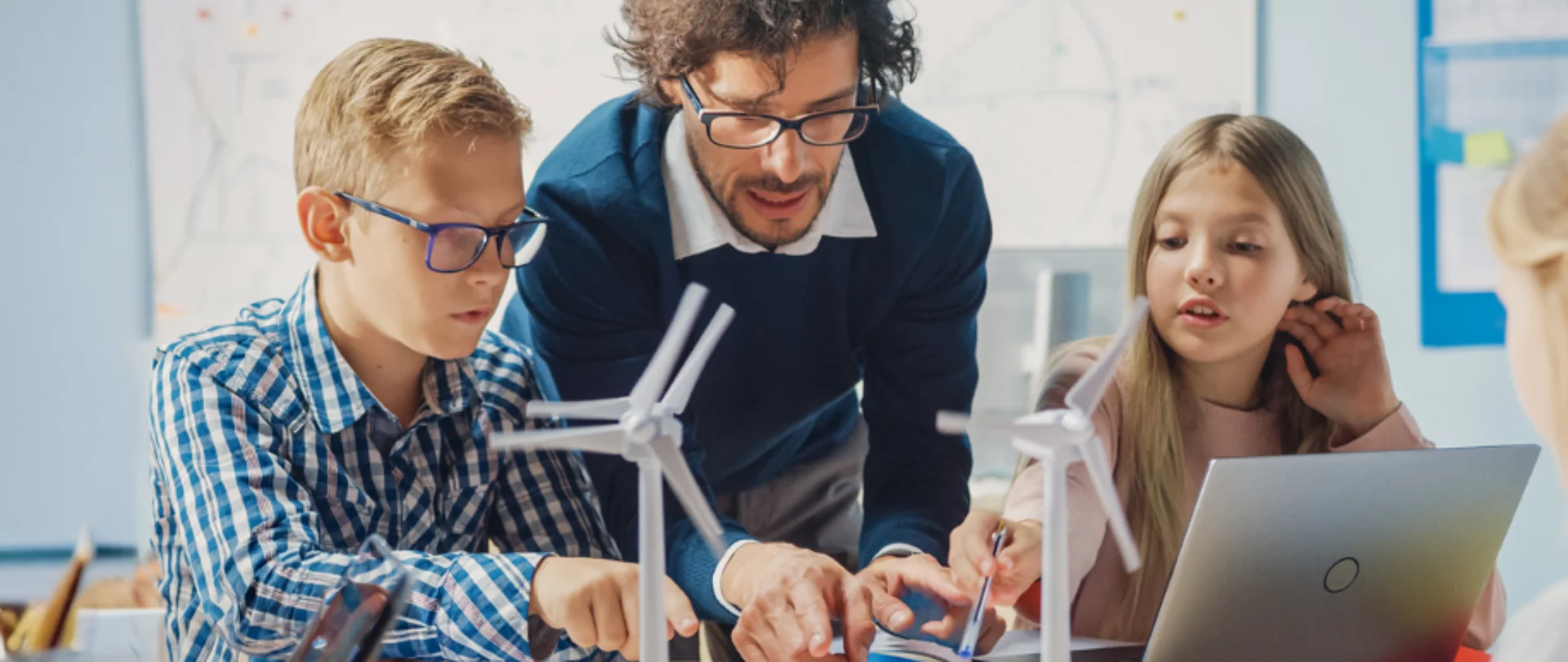Kinder arbeiten gemeinsam mit Lehrkraft an einem Energiewende-Projekt mit Windkraftmodellen und digitalen Lernmedien.