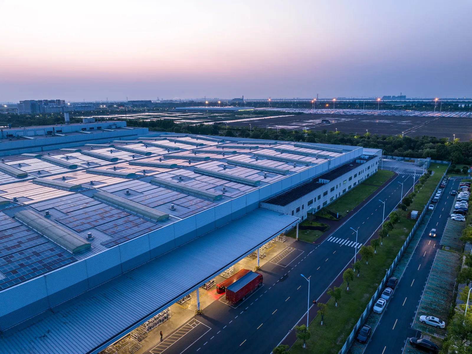 Eine Industriehalle mit Solarpaneelen auf dem Dach bei Sonnenuntergang, ein LKW steht davor.