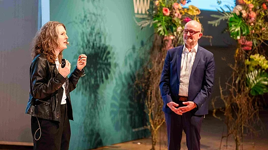 Anna Kopp im Austasuch mit Andreas Speith Anna Kopp und Andreas Speith auf einer Bühne bei der Veranstaltung Westfalen Weser Forum vor dekorierter Kulisse mit floralen Elementen.